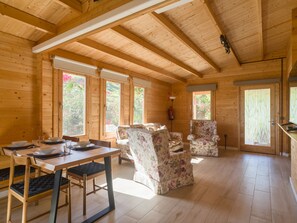 Interior de una cabaña de madera con una mesa de comedor, sillas y un ventanal grande.
