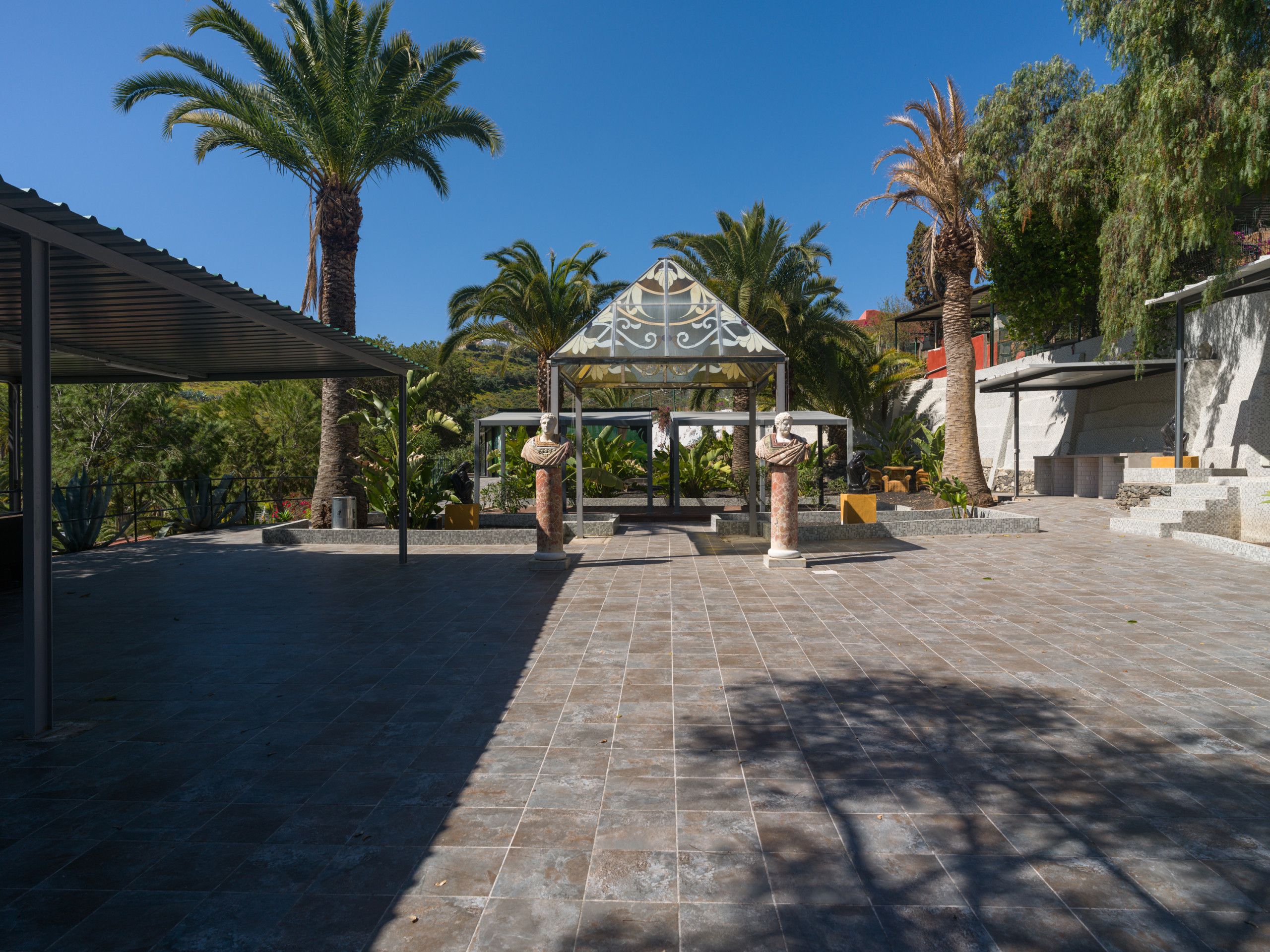 A courtyard with a gazebo, palm trees, and a statue.