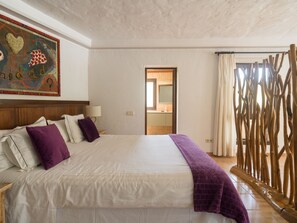 A hotel room with a large bed, a nightstand, a lamp, a painting on the wall, and a view of the outside through a window. - German Lofts by CanariasGetaway (Telde)
