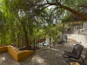 An outdoor patio with stone flooring, a wicker chair, and a view of a pool and stone wall. - German Lofts by CanariasGetaway (Telde)