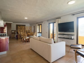 A living room with a sofa, a dining table with chairs, a TV mounted on the wall, and a kitchen area with a stove. - German Lofts by CanariasGetaway (Telde)