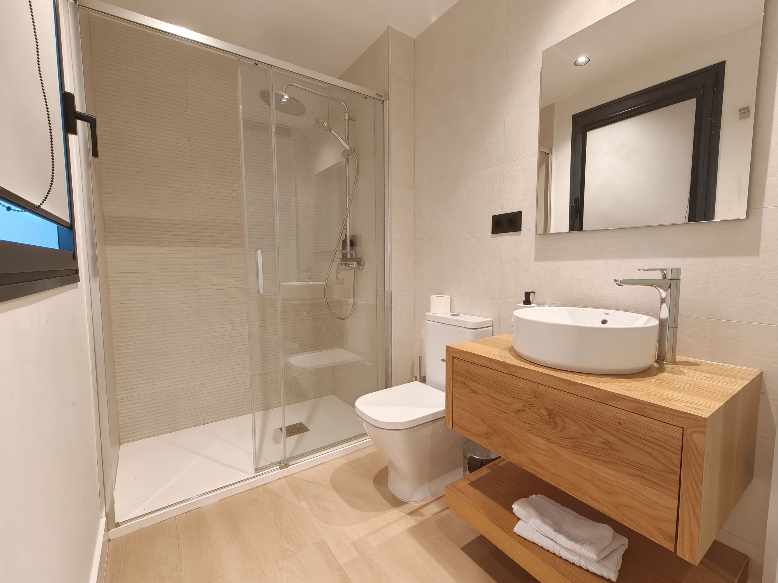 Une salle de bain moderne avec une douche à parois de verre, des toilettes blanches, un meuble-lavabo en bois et un miroir.