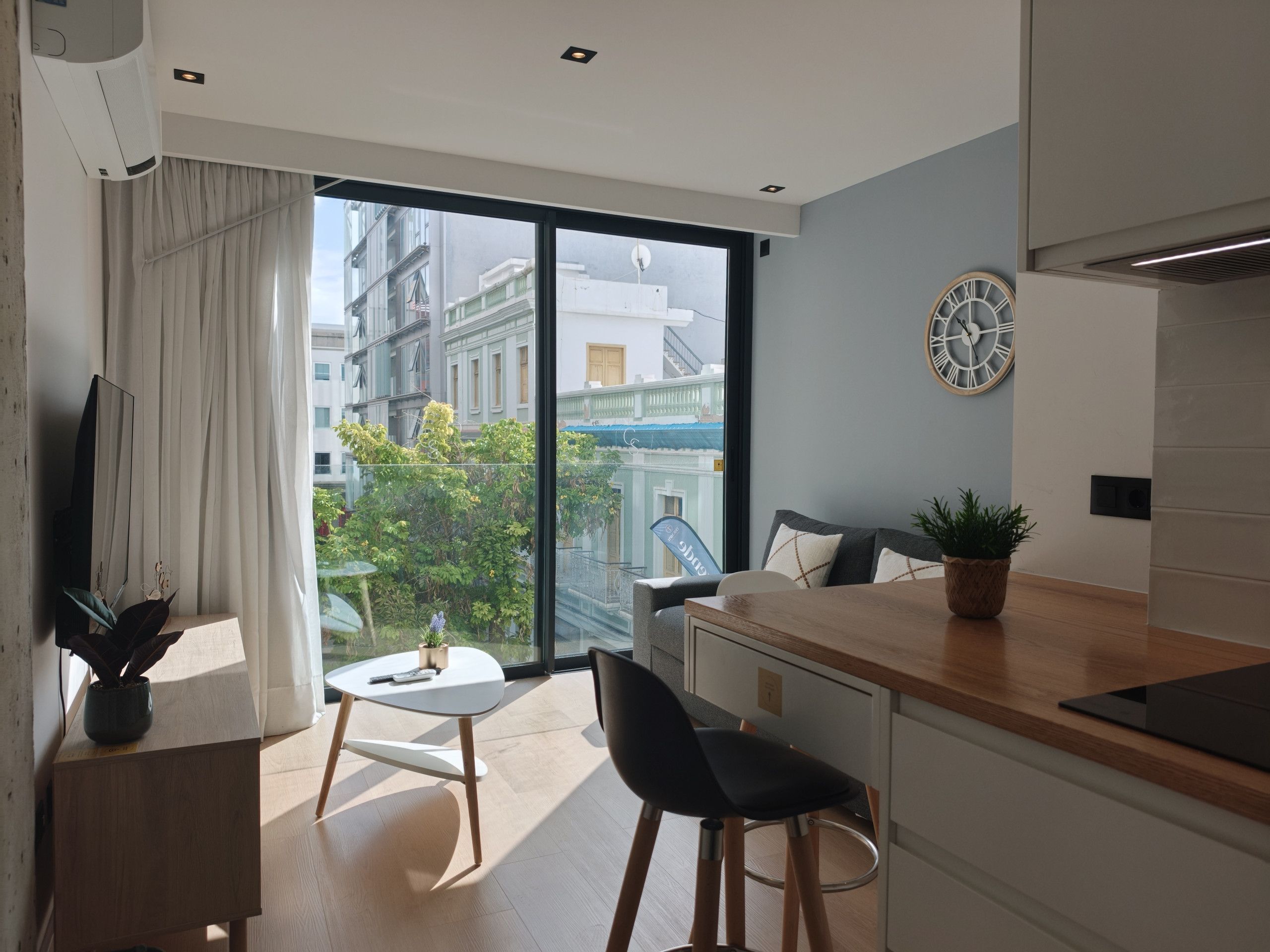 Une cuisine moderne dotée d’une grande fenêtre, un coin repas avec une table et des chaises, et un salon avec un canapé et un téléviseur.