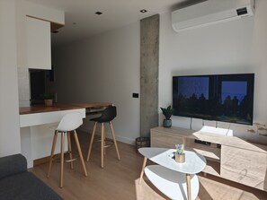 A modern living space with a kitchen area, a dining table with chairs, a TV mounted on the wall, and a small side table with a plant. - Costa Suites 49 2D by CanariasGetaway (Las Palmas de Gran Canaria)