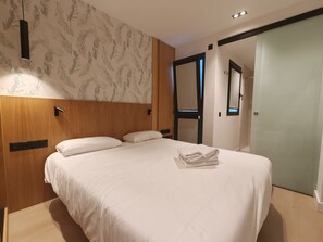 A hotel room with a bed, a wooden headboard, a wall-mounted light, and a door leading to another room. - Costa Suites 49 2D by CanariasGetaway (Las Palmas de Gran Canaria)