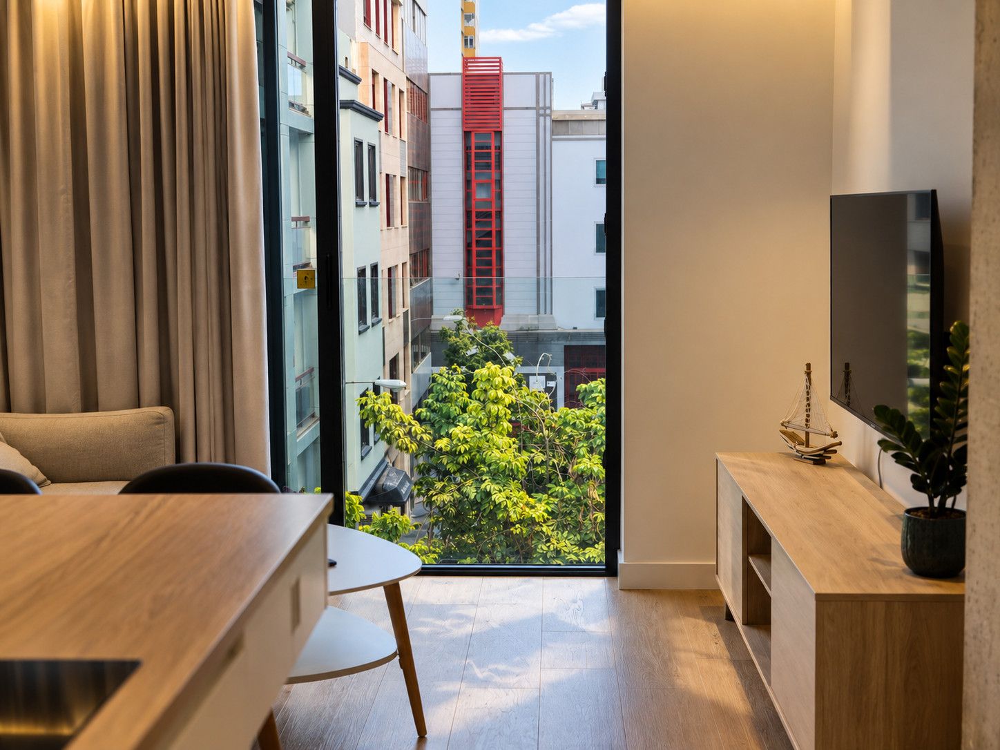 Un intérieur moderne comprenant un coin repas, un téléviseur fixé au mur et une vue sur le paysage urbain, visible à travers une grande fenêtre.