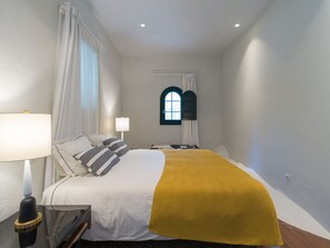 Een hotelkamer met een bed, twee bedlampen, een raam met gordijnen en een klein rondboogvenster.