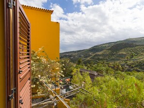 A yellow building with a wooden balcony overlooking a lush green landscape with hills. - Casa África Loft - Finca Cruz Mayor (Telde)