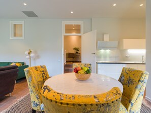 A dining area with a round table and yellow chairs, a bowl of fruit on the table, and a kitchen in the background. - Casa África Loft - Finca Cruz Mayor (Telde)