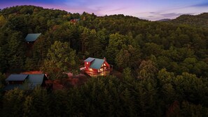 A cabin surrounded by dense forest, with a visible structure to the left and a smaller building to the right. - God`s Promise | Cozy, Peaceful, Hot Tub, Fireplace (Sevierville)