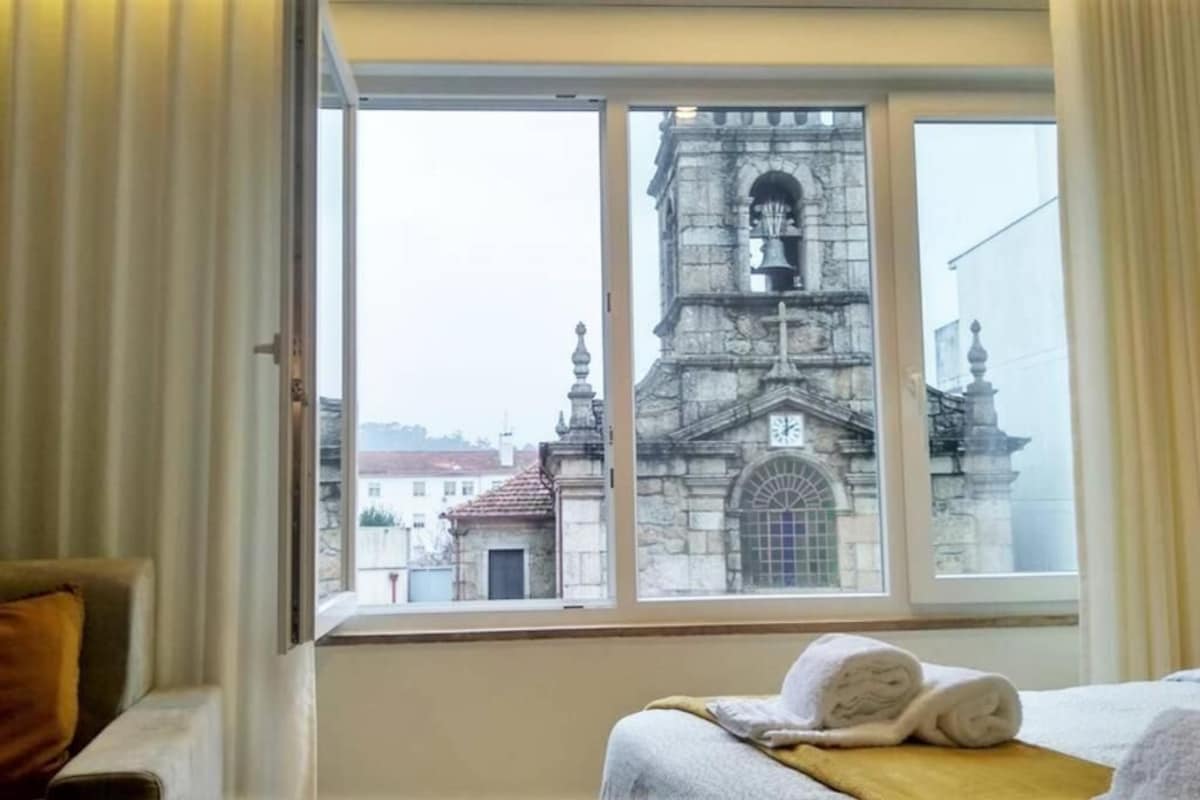 A hotel room with a large window, a bed with rolled towels, and a view of a historic building with a bell tower.