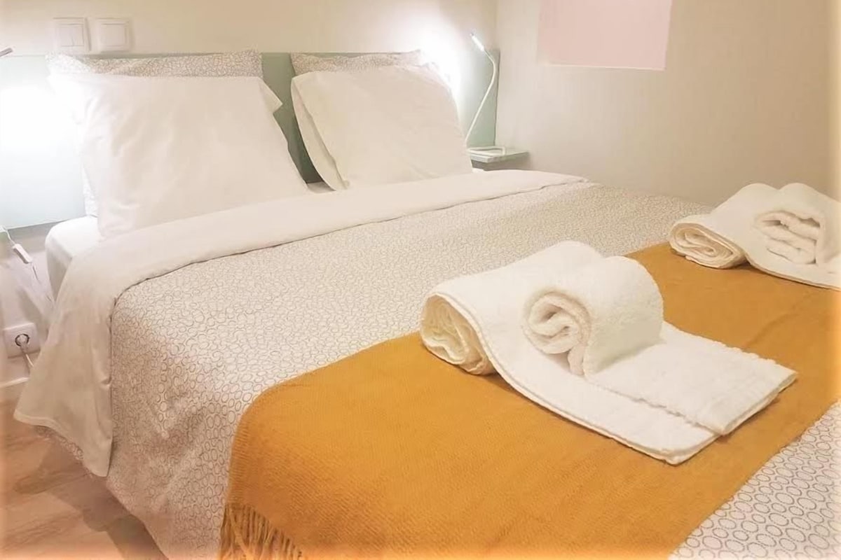A hotel room with a bed, pillows, a bedside table, and a lamp.