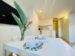 A modern dining area with a white table set for four, a vase with flowers, and a kitchen in the background. - Sweet Apartments (Vila Nova de Famalicão)