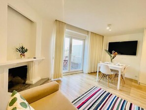 A modern living room with a fireplace, a dining area, and a large TV. - Sweet Apartments (Vila Nova de Famalicão)