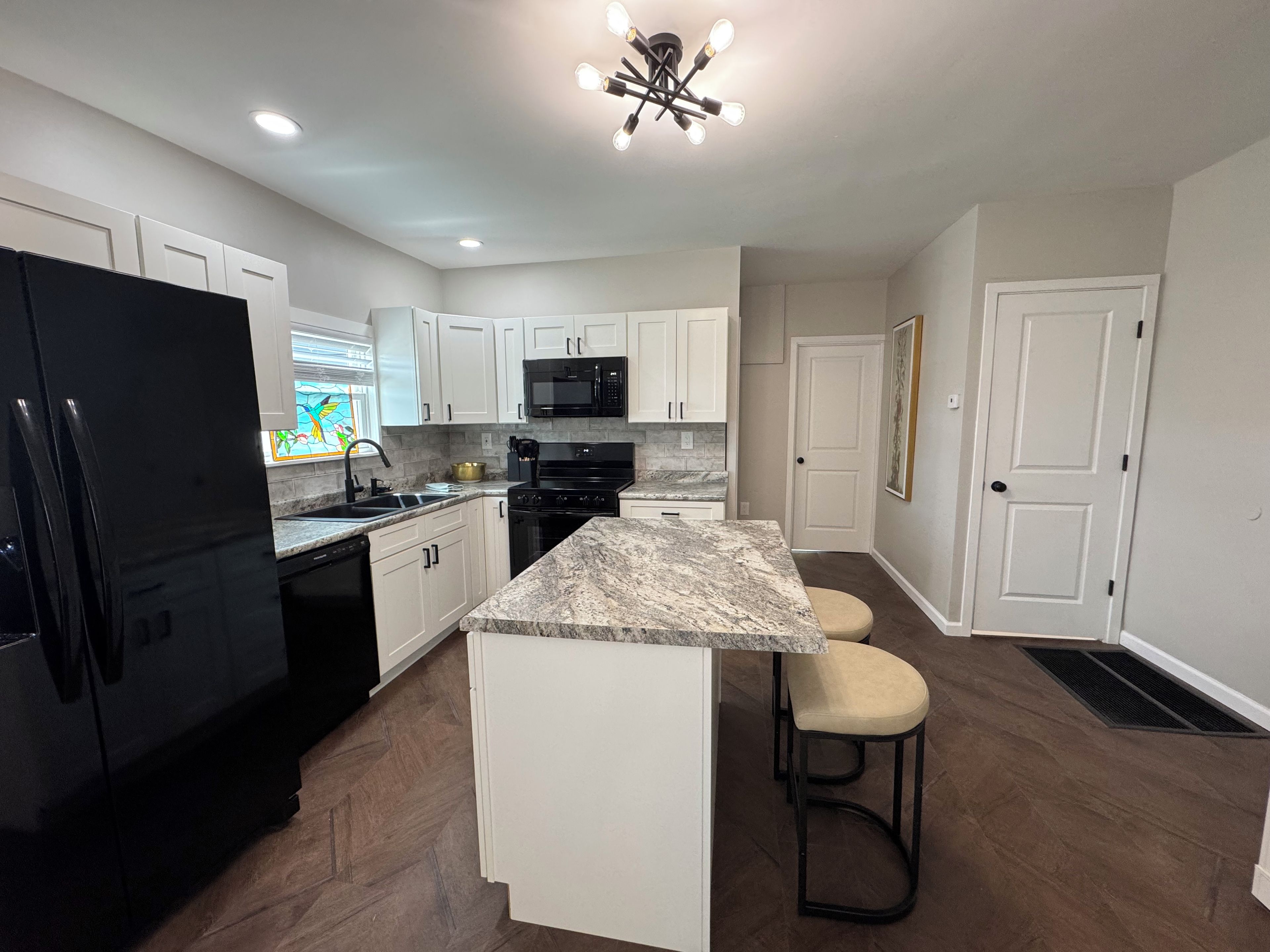 A modern kitchen with white cabinets, a black refrigerator, a granite countertop, and a stainless steel oven.