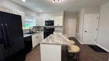 A modern kitchen with white cabinets, a black refrigerator, a granite countertop, and a stainless steel oven.