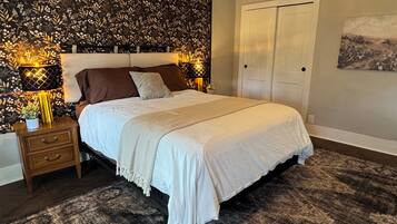 A bedroom with a bed, nightstands, a decorative wall panel, a door, and a rug.