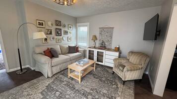 A living room with a sofa, armchair, coffee table, and a cabinet with decorative items.