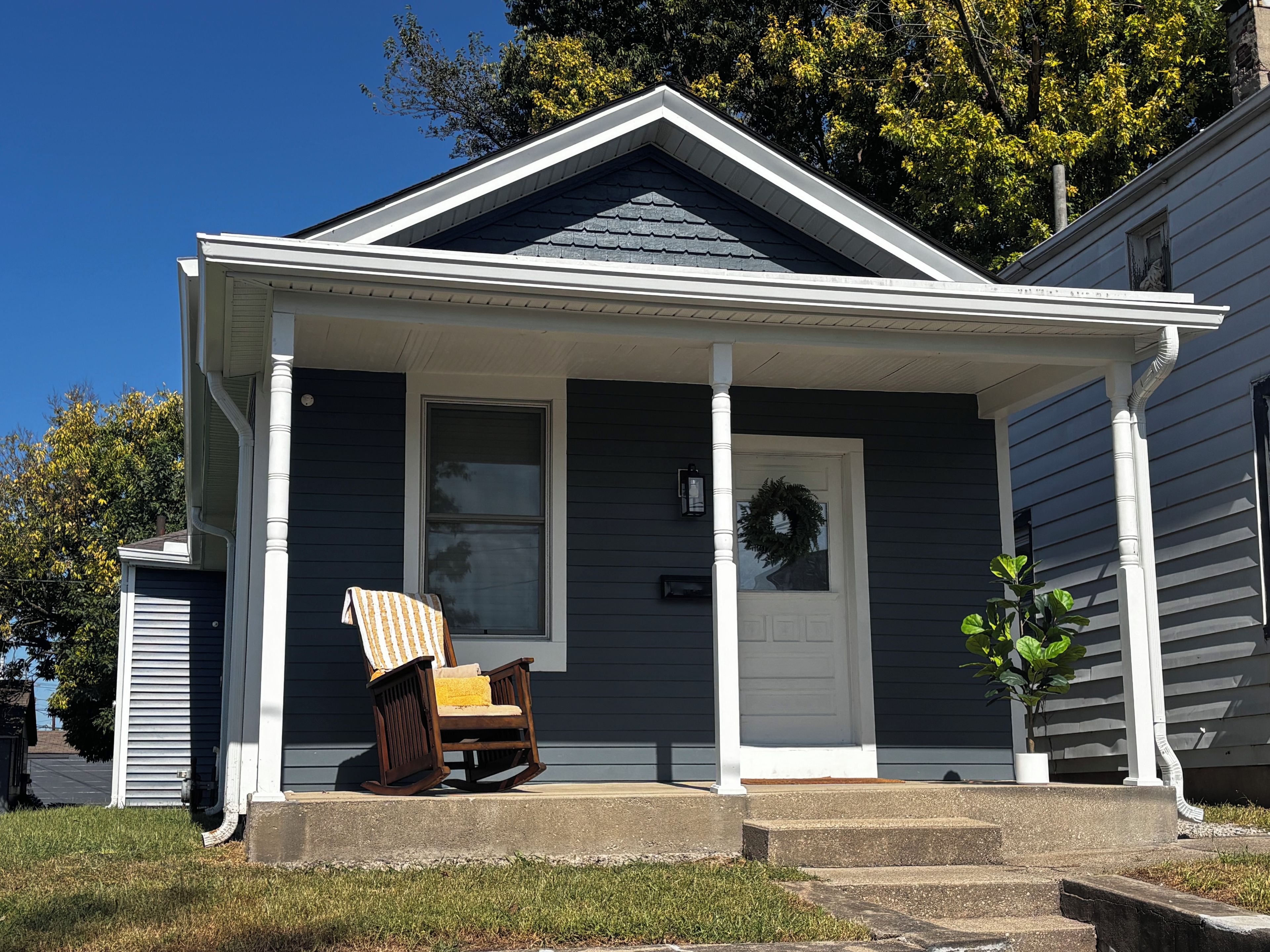A two-story house with a porch, a rocking chair, and a potted plant.