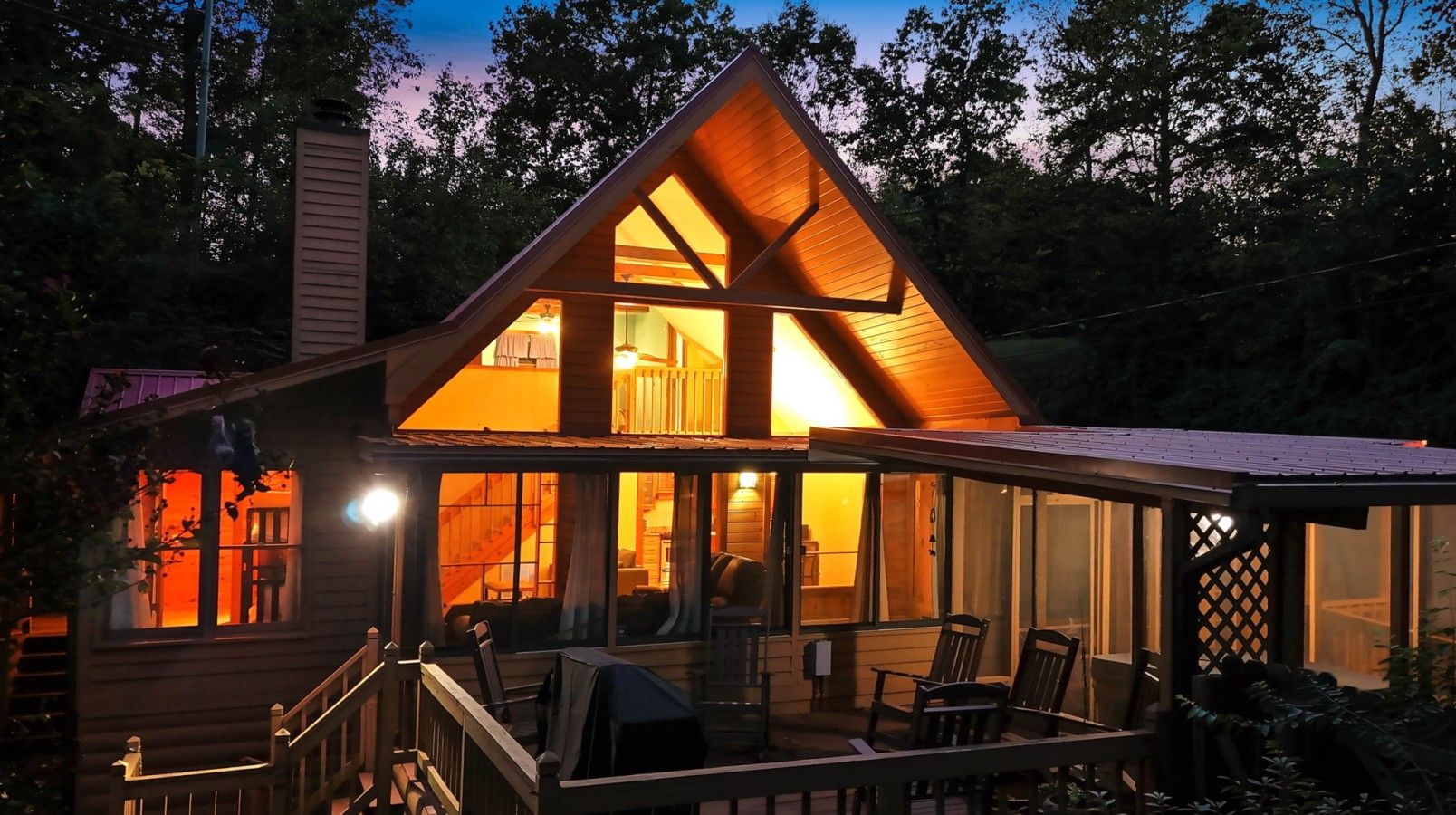 A wooden cabin with a large deck, multiple windows, and a staircase leading to the entrance.