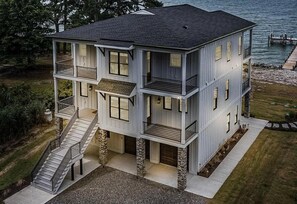 A multi-story building with a balcony on the second floor, a staircase leading to the entrance, and a dock extending into the water. - Grand Cove Sanctuary (Smith Mountain Lake)