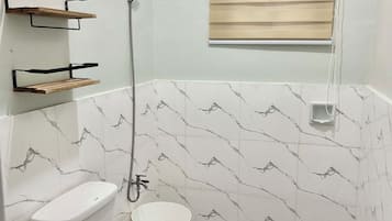 A bathroom with a toilet, a shower, and a window with blinds.