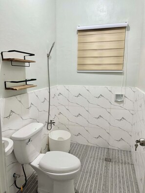 Ein Badezimmer mit Toilette, Dusche und einem Fenster mit Jalousien.