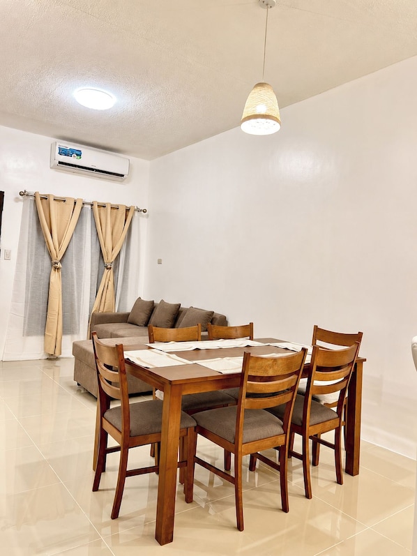 A dining area with a wooden table and chairs, a sofa, and curtains.