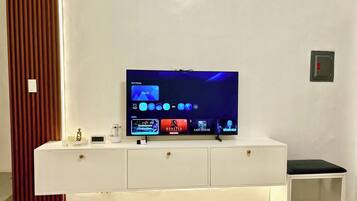 A modern living room with a flat-screen TV on a white entertainment unit, a small table, and a decorative item on the left.