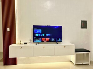 Ein modernes Wohnzimmer mit einem Flachbildfernseher auf einer weißen Unterhaltungsanlage, einem kleinen Tisch und einem dekorativen Gegenstand links.