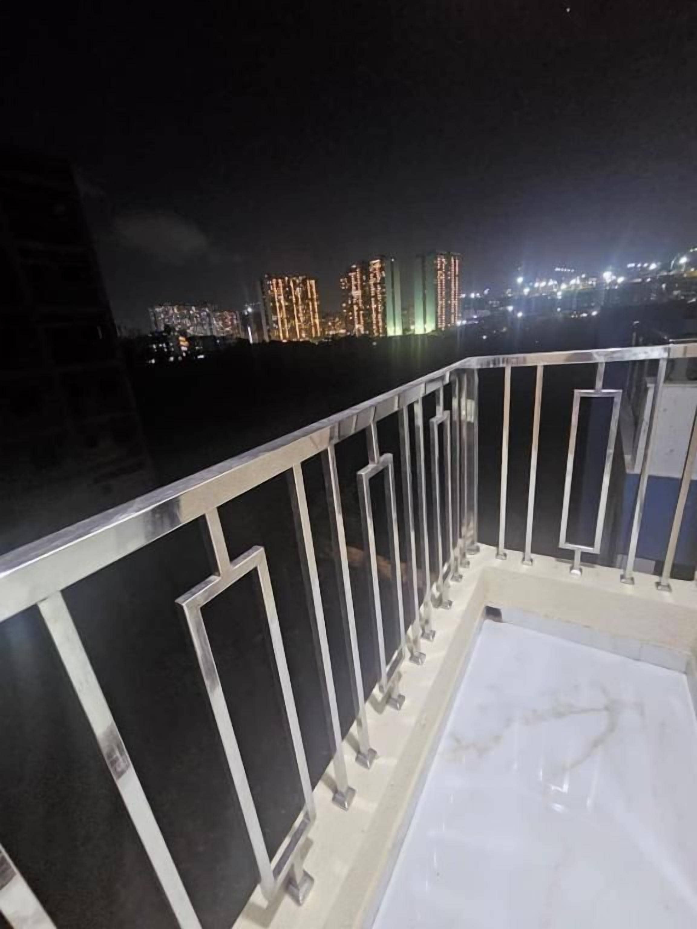 A balcony with a metal railing, a white floor, and a cityscape with illuminated buildings in the background.