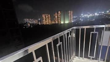 A balcony with a metal railing, a white floor, and a cityscape with illuminated buildings in the background.