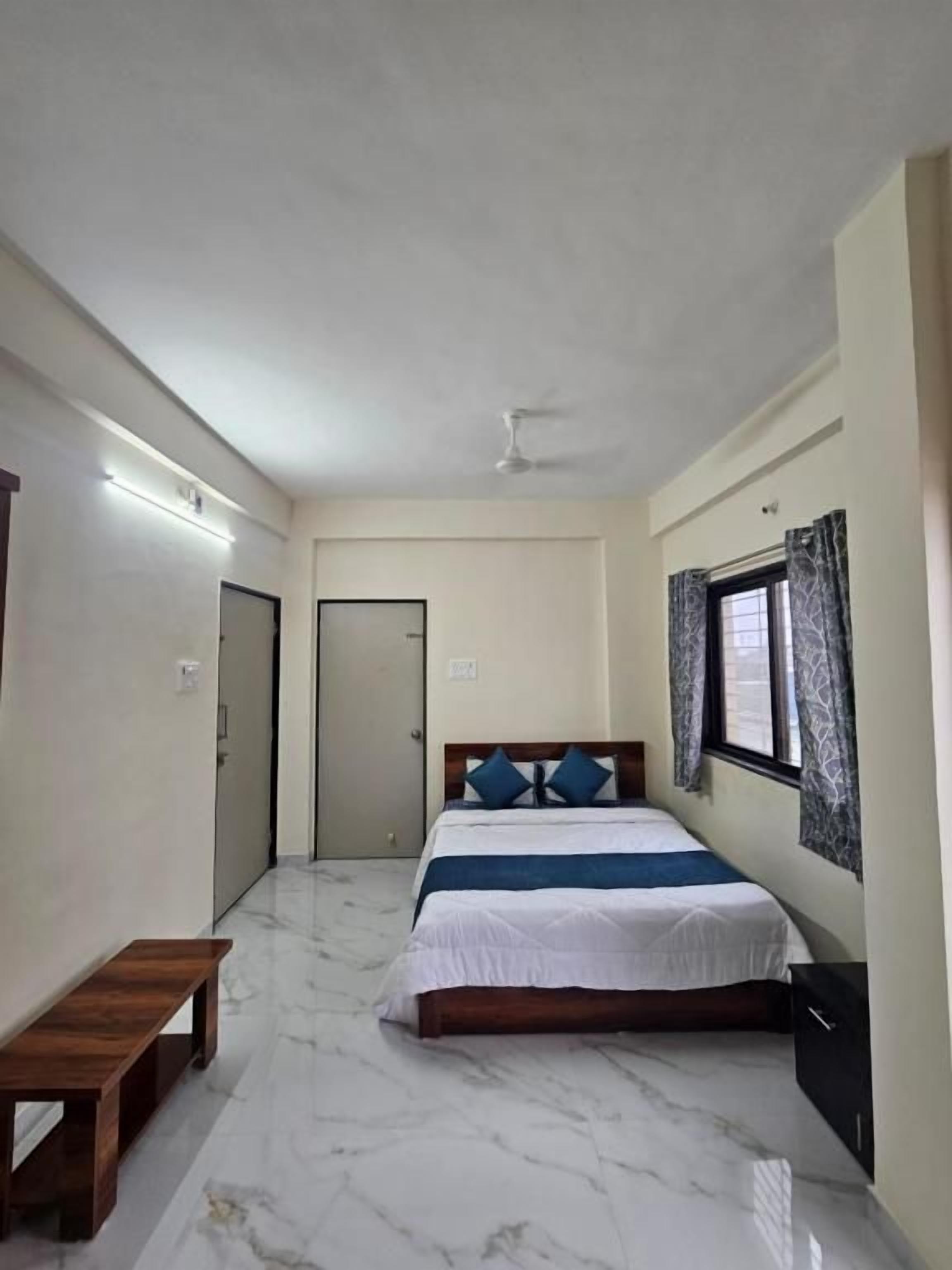 Une chambre à coucher comprenant un lit, un banc, une armoire, un ventilateur de plafond et une fenêtre avec des rideaux.