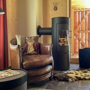 A cozy room with a leather armchair, a black wood-burning stove, and a fur rug on the floor. - Timber house with wellness area in Chiemgau (Unterwössen)