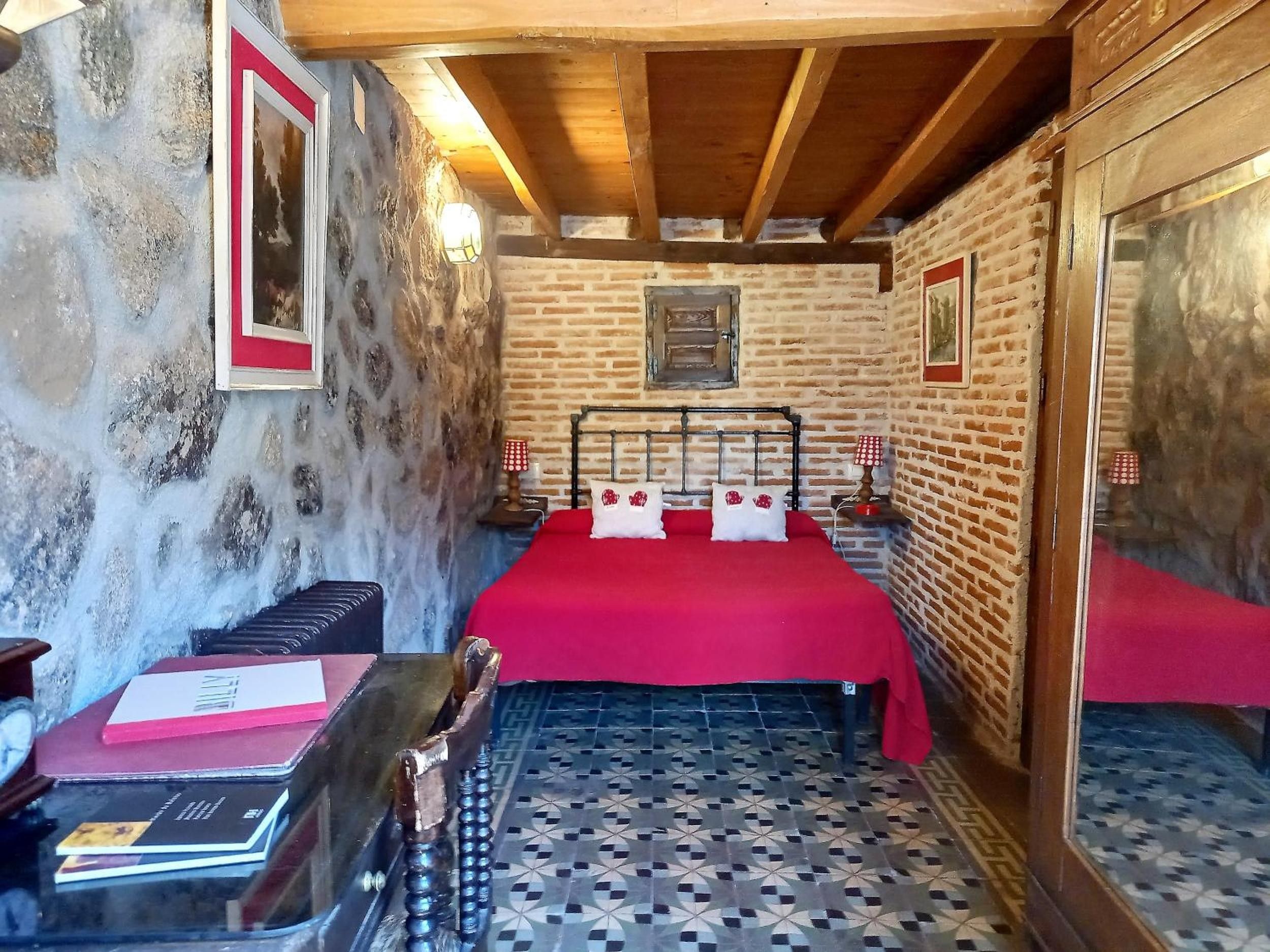 Een kamer met een bakstenen muur, een houten plafond, een bed met een rode sprei en een vloer met een patroon.