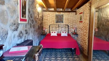 Een kamer met een bakstenen muur, een houten plafond, een bed met een rode sprei en een vloer met een patroon.