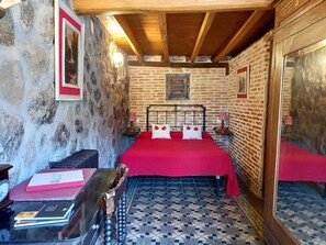 Een kamer met een bakstenen muur, een houten plafond, een bed met een rode sprei en een vloer met een patroon.