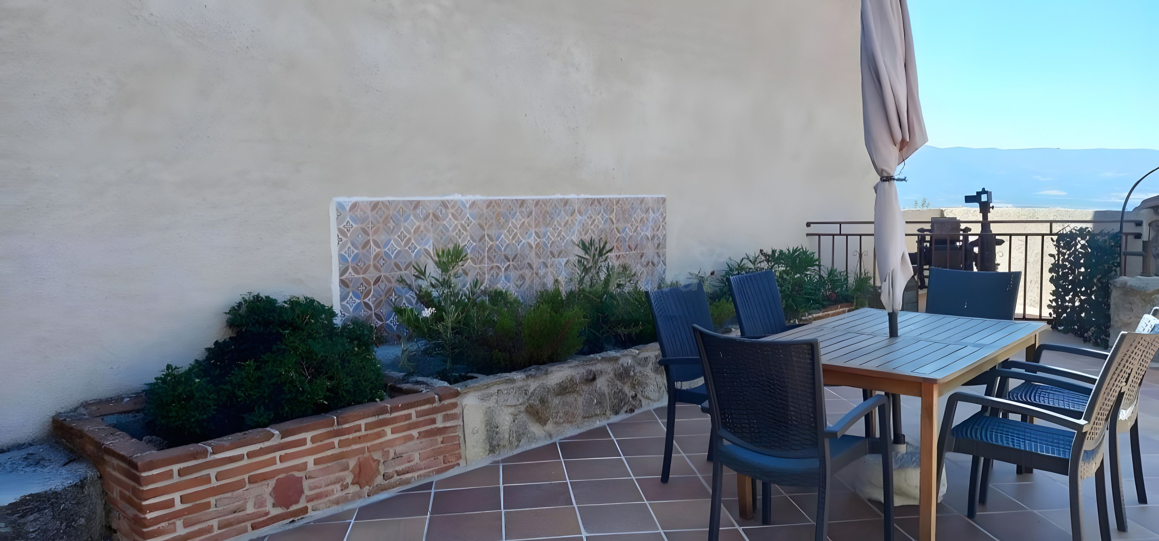 Een terras buiten met een tafel, stoelen, een bak uit baksteen en een decoratieve muur.