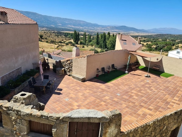 A rooftop patio with a view of the countryside, stone walls, and outdoor furniture.