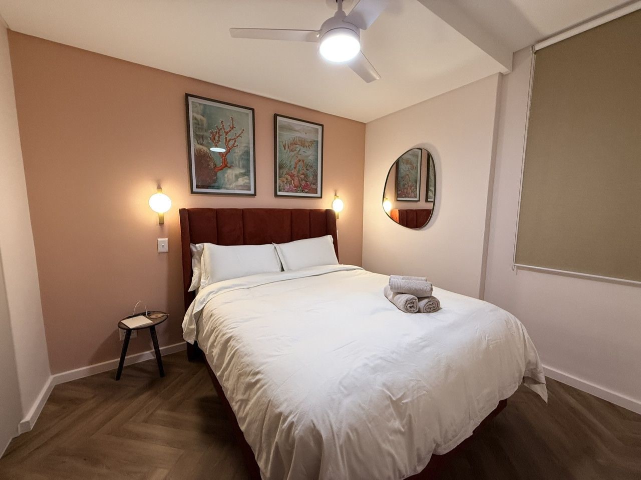A bedroom with a bed, a nightstand, a ceiling fan, wall-mounted lights, and artwork.