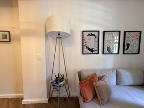 Un salon comprenant un canapé, une lampe sur pied et trois œuvres d’art encadrées accrochées au mur.