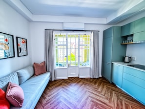 Ein modernes Wohnzimmer mit einer Couch, einem Essbereich mit Küchenzeile und einem großen Fenster mit Vorhängen.