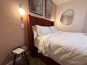 Une chambre à coucher comprenant un lit, une table de chevet, une lampe fixée au mur et deux œuvres d’art encadrées.