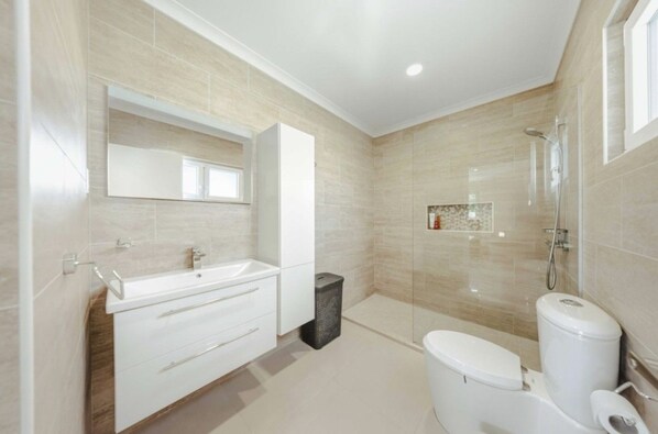 A modern bathroom with a white vanity, a glass shower enclosure, and a toilet. - Modern 4BR Palm Beach Home | Garden & BBQ (Noord)