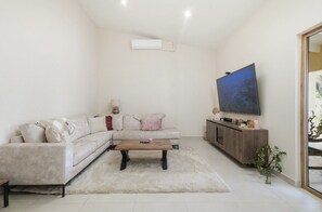 A modern living room with a sectional sofa, a coffee table, a TV on a stand, and a plant. - Modern 4BR Palm Beach Home | Garden & BBQ (Noord)