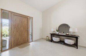 A room with a wooden door, a console table with lamps, a mirror, and a tiled floor. - Modern 4BR Palm Beach Home | Garden & BBQ (Noord)