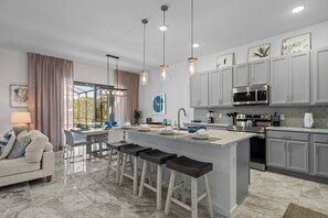 A modern kitchen with a central island, bar stools, stainless steel appliances, and pendant lighting. - 6BR Themed Villa • Private Pool • Near Universal (Orlando)