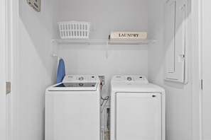A laundry room with two white washing machines, a blue iron, a white laundry basket, and a shelf with a 'Laundry' sign. - 6BR Themed Villa • Private Pool • Near Universal (Orlando)