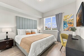 A modern bedroom with a bed, bedside tables, a desk, a chair, a window with curtains, and artwork on the wall. - Vista Cay 3BR Condo • Pools • Near Universal (Orlando)