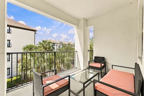 A balcony with a glass table and chairs, a view of neighboring buildings, and a clear sky. - Vista Cay 3BR Condo • Pools • Near Universal (Orlando)